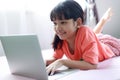 Portrait shot little Asian girl using a laptop computer to learn from home and laying on the bed with happiness, self-quarantine