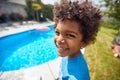 Portrait shot of lovely african american boy standing by the outdoor in ground pool in the backyard, smiling and feeling happy Royalty Free Stock Photo