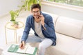 Casual businessman sitting on the couch at home while making a call and taking notes on notepad Royalty Free Stock Photo