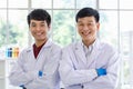 Portrait shot of two Asian professional male scientists in white lab coat and rubber gloves standing crossed arms smiling look at Royalty Free Stock Photo