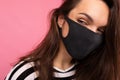 Portrait shot of young attractive woman wearing mediacal black face mask isolated over background wall