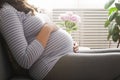 Portrait shot of young beautiful woman on third trimester of pregnancy. Close up of pregnant female with arms on her round belly.