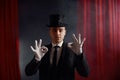 Portrait of showman in top hat and tailcoat against red curtain on background