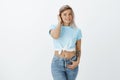 Portrait of shy and cute attractive female student in cropped top with tattoos and pierced belly, touching hair strand Royalty Free Stock Photo