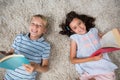 Portrait of siblings lying on rug and reading book in living room