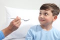 Portrait of sick child looking at nurse giving him medicine with spoon