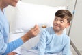 Portrait of sick child looking at nurse giving him medicine with spoon