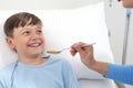 Portrait of sick child looking at nurse smiling and her giving him medicine with spoon