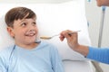 Portrait of sick child looking at nurse smiling and her giving him medicine with spoon