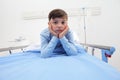 Portrait of sick child sitting in bed alone in hospital room thinking to his disease with copy space