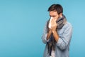 Portrait of sick man standing wrapped in warm scarf sneezing in napkin, feeling unwell suffering seasonal influenza