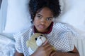 Portrait of sick mixed race girl lying in hospital bed holding teddy bear Royalty Free Stock Photo