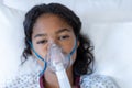Portrait of sick mixed race girl lying in hospital bed wearing oxygen mask ventilator Royalty Free Stock Photo
