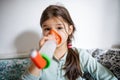 Portrait of sick small girl at home, using inhaler.