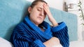 Closeup portrait of sick woman with flue measuring temperature and holding hand on aching head