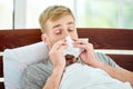 Portrait of a sick young man with runny nose suffering from cold or flu and sneezing while lying in bed at home. Virus Royalty Free Stock Photo