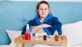 Portrait of sick young woman with fever lying in bed with tray full of medicines