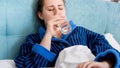 Portrait of sick young woman lying in bed and drinking water from glass Royalty Free Stock Photo