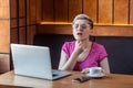 Portrait of sickness young adult woman with short blonde hair in pink t-shirt and eyeglasses sitting in cafe and touching throat