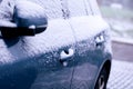A portrait of the side doors and the wing mirror of a car getting completely snowed under during a snowstorm. The vehicle is