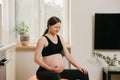 A pregnant woman is writhing in pain with her arm on belly on an exercise ball