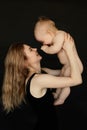 Portrait side view of young smiling mother raise and play with cute naked baby on black background. Happy parent