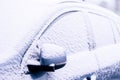 A portrait of the side windows and the wing mirror of a car getting completely snowed under during a snowstorm. The vehicle is