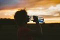 Portrait of a silhouette of a young tourist woman drinking water from a transparent blue bottle in a field, jars at sunset. The gi Royalty Free Stock Photo