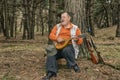 Portrait of singing senior hunter resting in evening forest and playing mandolin