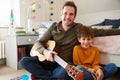 Portrait Of Single Father At Home With Son Playing Acoustic Guitar In Bedroom