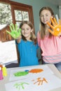 Portrait of sisters with paint covered hands and colorful handprints on papers