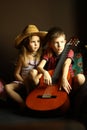 Portrait of sitting caucasian children, wearing western style straw hat and holding guitar Royalty Free Stock Photo