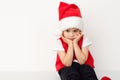 Portrait of sitting resentful little child in red Santa Claus hat isolated on white background. Beautiful five-year European boy.