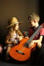 Portrait of sitting and smiling at each other caucasian children, wearing western style straw hat and holding the guitar Royalty Free Stock Photo