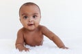 Portrait of a six month crawling African American baby on fluffy white rug, happy smiling adorable sweet little girl kid lying on