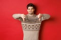 Portrait of skeptical and disappointed handsome man in christmas sweater, dislike new year party, showing thumbs-down