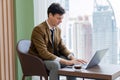 Skilled businessman working with laptop near window with skyscraper. Ornamented. Royalty Free Stock Photo