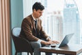 Skilled businessman working with laptop near window with skyscraper. Ornamented. Royalty Free Stock Photo