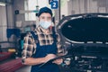Portrait of skilled guy mechanic writing list car repair maintenance wearing gauze mask goggles in garage Royalty Free Stock Photo
