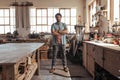 Skilled young woodworker standing in his workshop full of tools