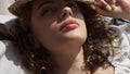 Portrait sleepy girl covering curly head with hat from sunlight lying beach.