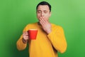 Portrait of sleepy dreamy guy drink coffee yawn palm cover mouth on green background