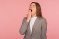 Portrait of sleepy exhausted young woman in business suit yawning lovely, covering mouth with hand