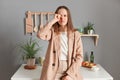 Portrait of sleepy tired brown haired woman wearing beige suit standing near table on kitchen at home, rubbing eyes, feels fatigue