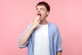 Portrait of sleepy tired male student or worker in casual striped shirt yawning. isolated on pink background