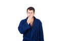 Portrait of sleepy young man messy hair, wears blue bathrobe yawning, covering his mouth with hand isolated on white background Royalty Free Stock Photo