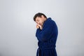 Portrait of sleepy young man wearing blue bathrobe holding hand to forehead, eyes closed feel tired needs to sleep isolated on Royalty Free Stock Photo