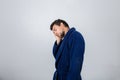 Portrait of sleepy young man wears blue bathrobe holding hand to forehead, eyes closed feel tired needs to sleep isolated on white Royalty Free Stock Photo
