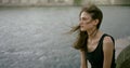 Portrait of a Slender dark-haired girl model in a short black dress sitting on a tile near the city river, the wind