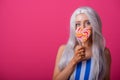 Portrait of a slender woman in a blonde wig posing with a lollipop on a pink background. Cute girl with blue eyes in a Royalty Free Stock Photo